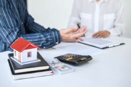 people reviewing homeowners insurance documents next to a calculator, money, and model home